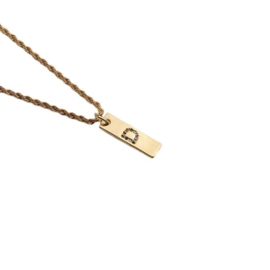 Detail of gold pendant necklace with colorful cubic zirconia letter D on a rope chain