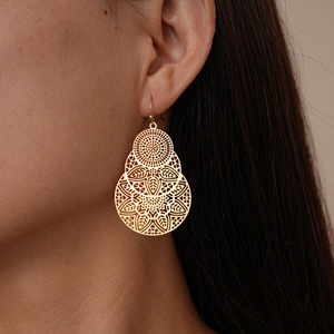 Gros plan sur des boucles d'oreilles fleurs dorées ajourées portées par un mannequin