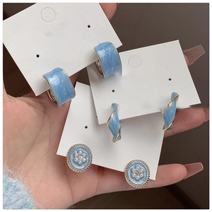 Detail view of blue enamel earring set with gold accents, pearls, and crystals in hand