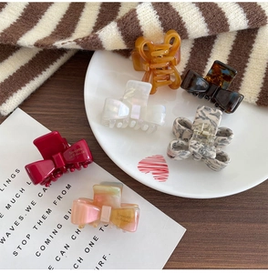 Close-up of six colorful acetate bow hair claws on a decorative heart-shaped ceramic tray