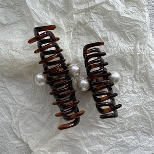 Detail of tortoise shell claw clips with pearl accents on a white textured backdrop