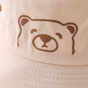 Close-up of beige cotton bucket hat featuring embroidered cartoon bear face and fine stitching
