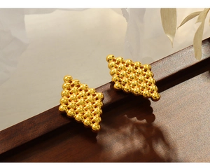 Detailed macro view of vintage geometric gold bead stud earrings on a dark wood stand