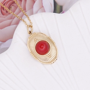 Detail of bohemian gold irregular oval necklace featuring a red gemstone and sunburst texture