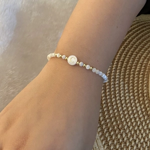 Close-up of white beaded bracelet featuring a gold letter C charm on a model wrist