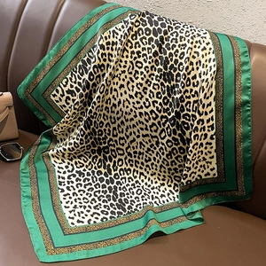 Detail of leopard print silk scarf with dark green border draped on a leather sofa