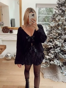 Détail du cardigan noir à paillettes avec col en V et petits nœuds et short assorti