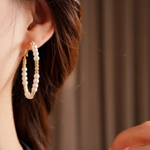 Close-up of elegant gold beaded pearl hoop earrings worn by a model in soft lighting