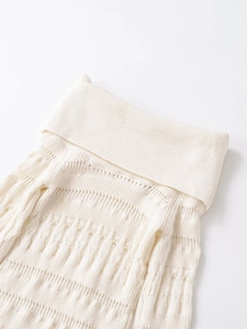 Detail shot of white knit sweater showing intricate hollow patterns and folded collar