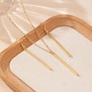 Minimalist gold geometric rectangular bar necklace and earrings set on wooden tray