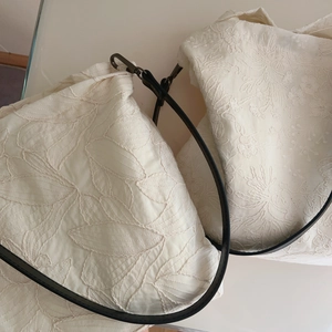 Close-up of beige cotton tote bag with intricate floral embroidery and leather strap