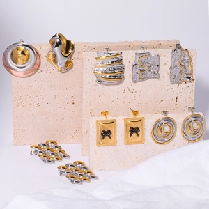 Mixed gold and silver geometric earrings with bow and pleated texture on beige stone