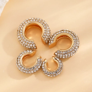 Set of 4 gold C-shaped ear cuffs with pavé white rhinestones on beige background