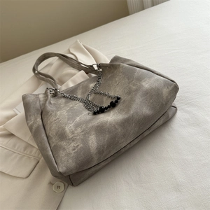 Large gray tote bag with vintage texture and silver chain detail on a white blazer