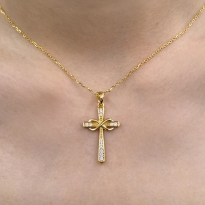 Detailed close-up of golden infinity cross necklace with white diamonds on a model