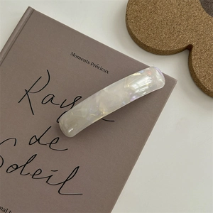 Fermaglio per capelli in resina bianca iridescente su un libro con luce naturale