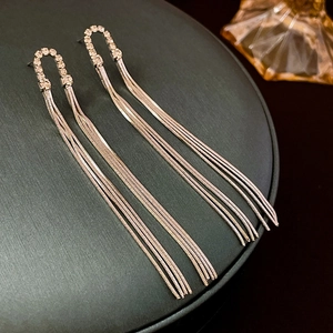 Macro detail of silver tassel earrings with geometric crystal studs on grey stand