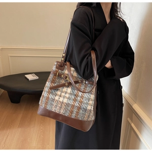 Detail of tweed and leather patchwork shoulder bag with golden buckle on a model