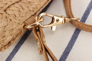Macro view of gold lobster clasp and woven texture on striped straw crossbody bag