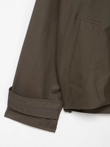 Detailed close-up of waterproof trench coat cuff and pocket in olive twill fabric