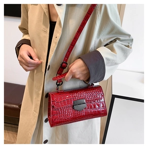 Detail of red crocodile texture handbag with black hardware on beige trench coat