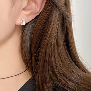 Detail of a silver pear-shaped stud earring with an iridescent gemstone on a model's ear