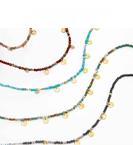 Macro detail of colorful beaded necklaces featuring small gold disc pendants and faceted stones