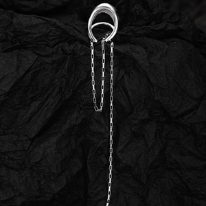 Detail of silver irregular ear cuff with long chain tassel on a black textured background