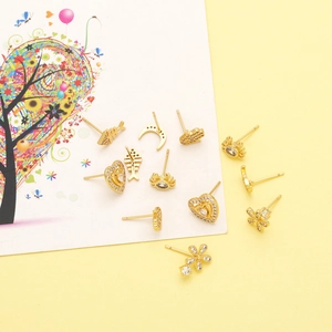 Detailed flat lay of golden stud earrings featuring fishbone, heart, and crab shapes with zircons
