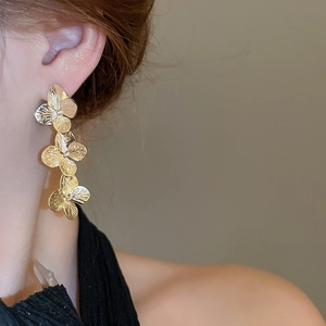 Macro view of triple gold flower earrings on model highlighting delicate petal details