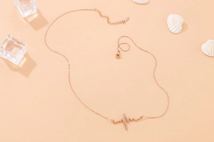 Macro shot of rose gold heartbeat necklace with shells and ice cubes on orange background