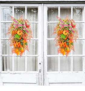Detail of autumn wreath with orange pumpkins, maple leaves, and red plaid bow on white door