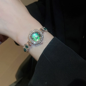 Close-up of elegant gold watch with green dial and diamond-set bracelet on wrist