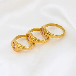 Detailed view of three gold rings with square pink zircons on soft white silk fabric