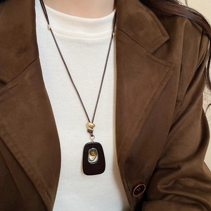Macro shot of oval tiger eye resin pendant necklace with gold bead on vintage sweater chain