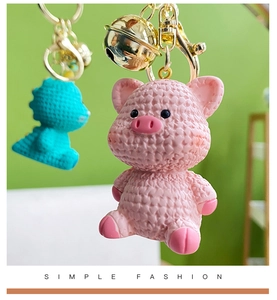 Close-up of cute pink pig keychain with realistic knitted texture and golden bell