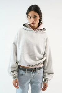 Detail of leopard print cuffs and distressed ripped hem on grey hooded sweatshirt