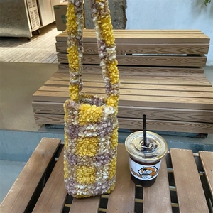 Detailed knit checkered water bottle bag in yellow and brown at an outdoor cafe
