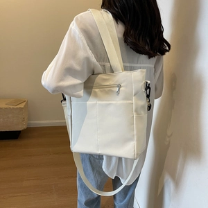 White canvas shoulder bag with wide strap and external pocket, worn by model in soft light