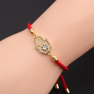 Detail of red braided rope bracelet with golden Hamsa hand and zircon evil eye charm