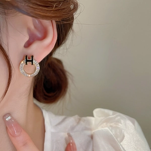 Macro shot of gold hoop earrings with white zircon and black H emblem on a model