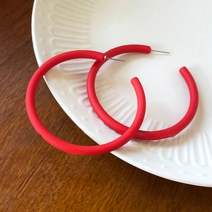 Detailed close-up of red matte acrylic C-shaped hoop earrings on a ceramic dish