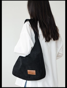 Detail of black corduroy shoulder bag showing vertical texture and brown leather patch