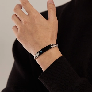 Close-up of a black rectangular tag bracelet with a silver cross and blue sapphire detail