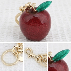 Sparkling red apple keychain with golden clasp and glitter leaf on textured background