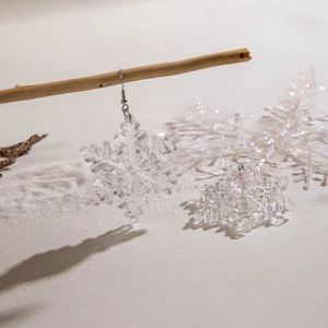 Close-up of transparent resin snowflake earrings hanging on a snowy winter branch