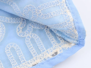 Detailed close-up of blue fabric with white geometric wave lace embroidery and hem