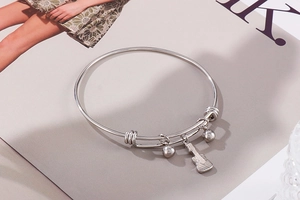Detailed shot of polished silver stainless steel bangle with guitar charm and round beads