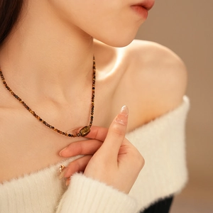 Detail of tiger eye stone pendant on a brown beaded necklace worn by a model