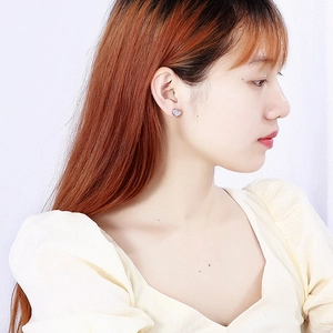 Close-up of minimalist silver heart earring with white shell inlay on model's ear